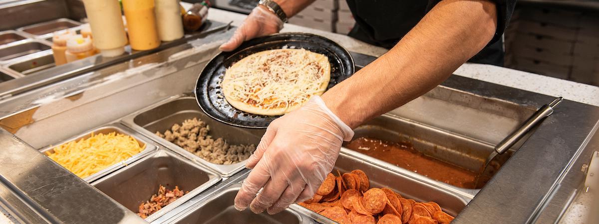 Dining services employee making a pizza.